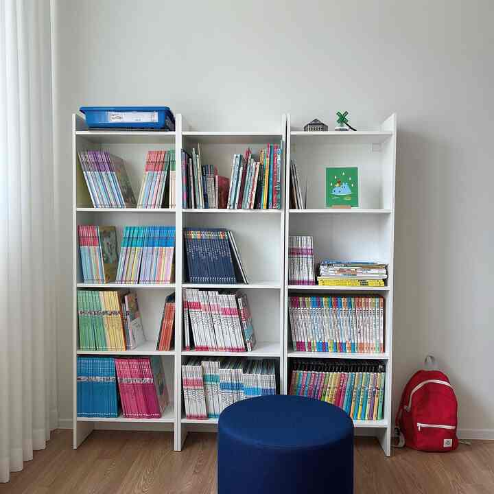 白い壁と木目調の床の子供読書コーナー、白い本棚と青いスツール、赤いリュックが配置された清潔感のあるインテリア