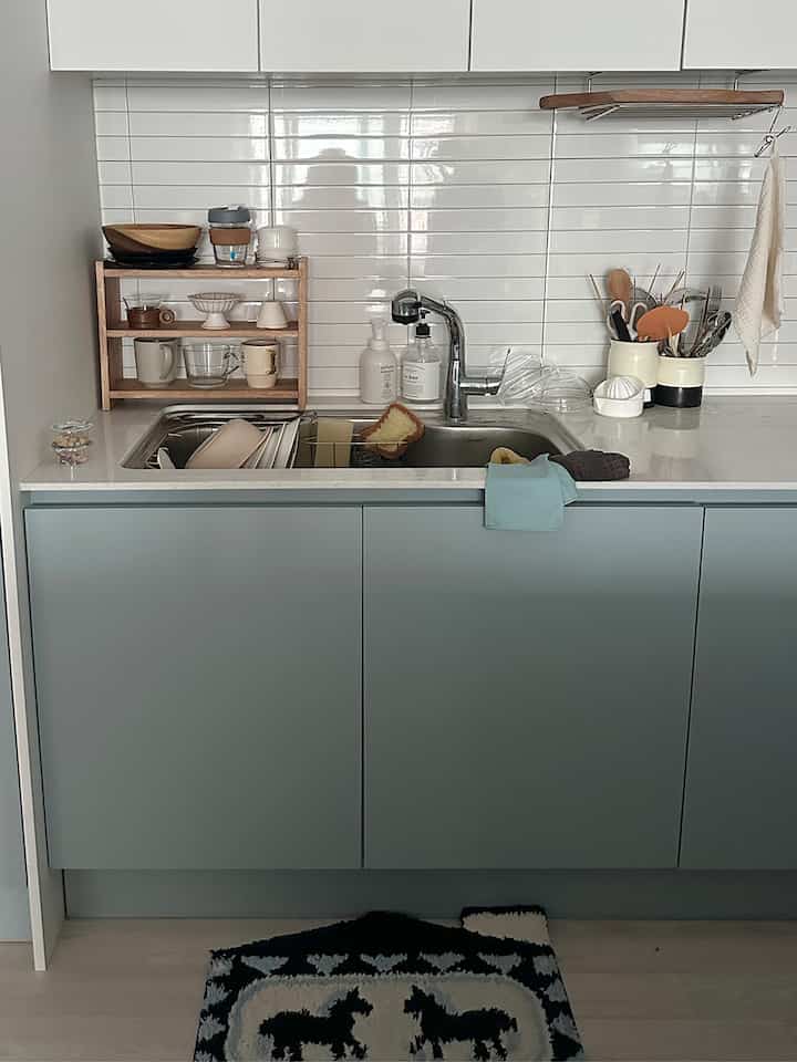 白いタイル壁と明るいナチュラルカラーの下部収納があるシンプルで整ったキッチン