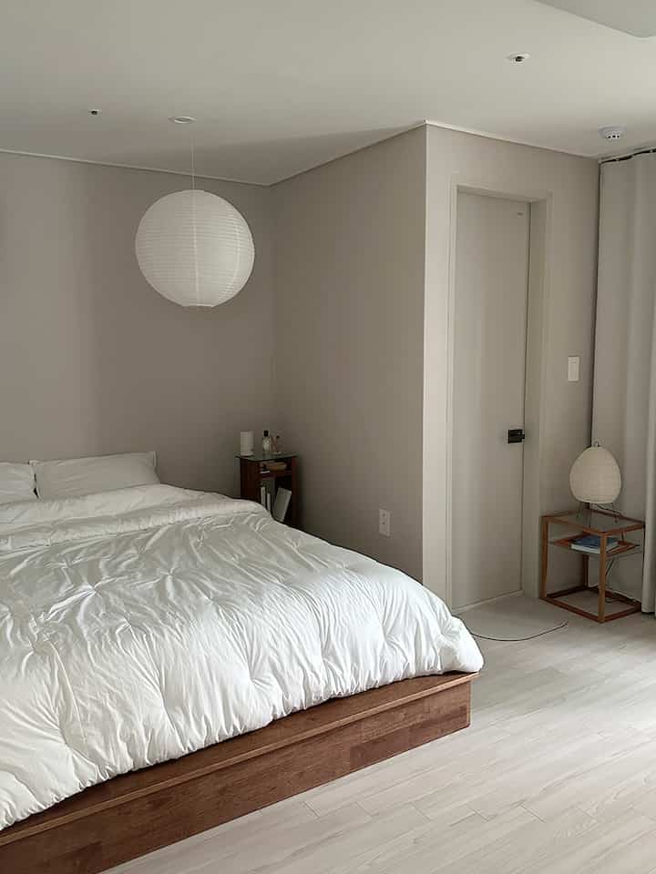 ナチュラルカラーと木目調の寝室、シンプルなベッドと照明が配置されたモダンな空間