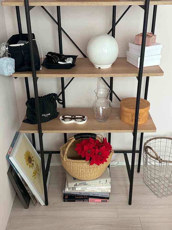 白い壁と木目調の棚が中央に配置された玄関またはリビングの整った収納スペース、黒い金属フレームと多様な小物が調和した空間