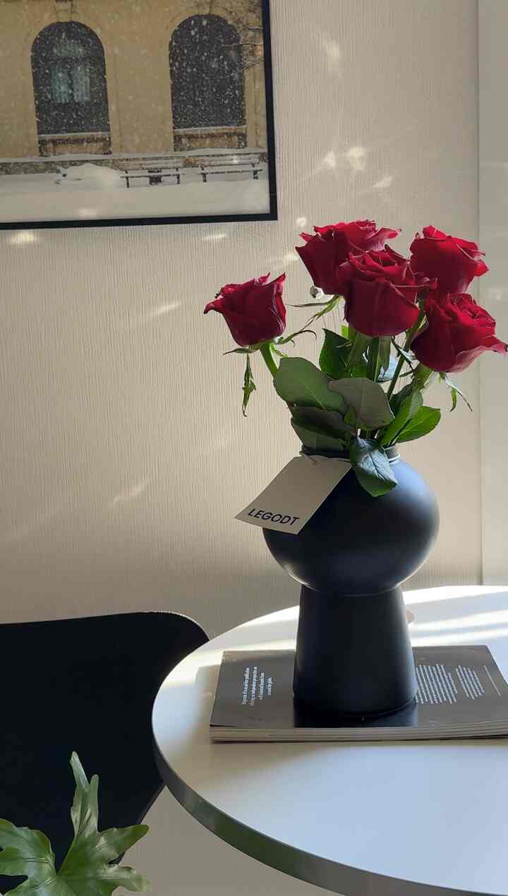 ベージュの壁と白い丸テーブルがあるキッチンスペース。黒い花瓶に赤いバラが生けられ、明るく温かみのある雰囲気のインテリア