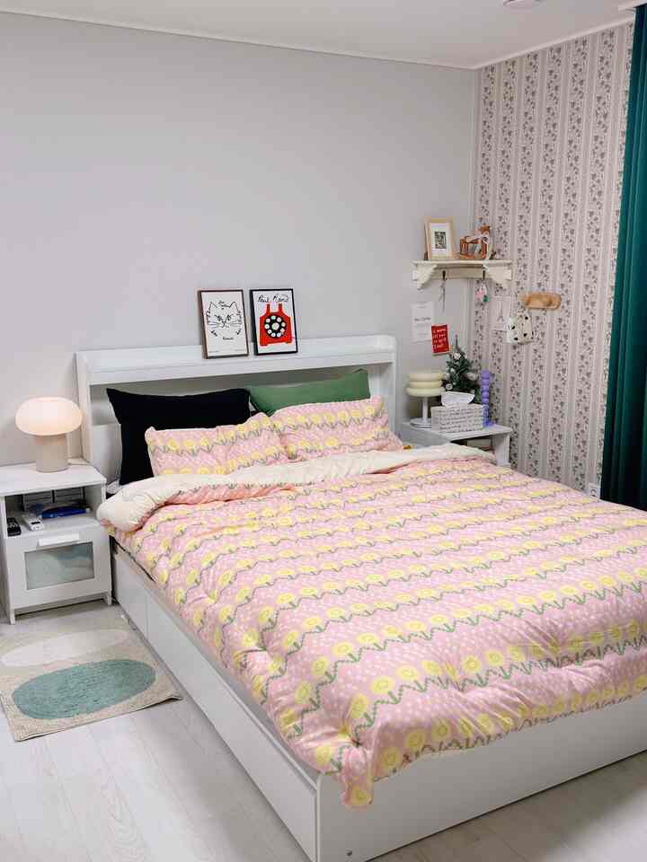 白とピンクの寝具が印象的な寝室、低い収納ベッドとヴィンテージ風の壁紙が調和した居心地のよいインテリア