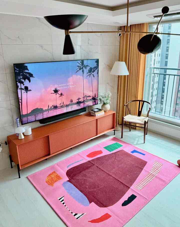 ピンクとオレンジのアクセントが際立つモダンなリビング、テレビ台とカラフルなラグが調和した空間