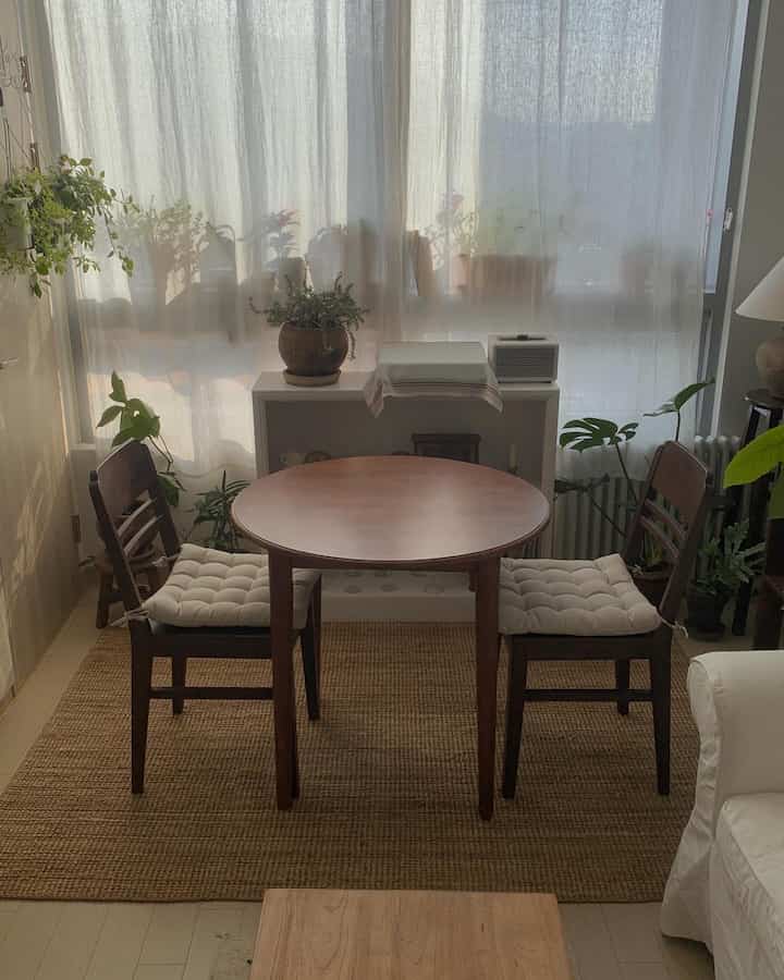 ナチュラルな色調のダイニングルーム、木製の円形テーブルと椅子、リネンカーテン、植物が配置された雰囲気のあるインテリア