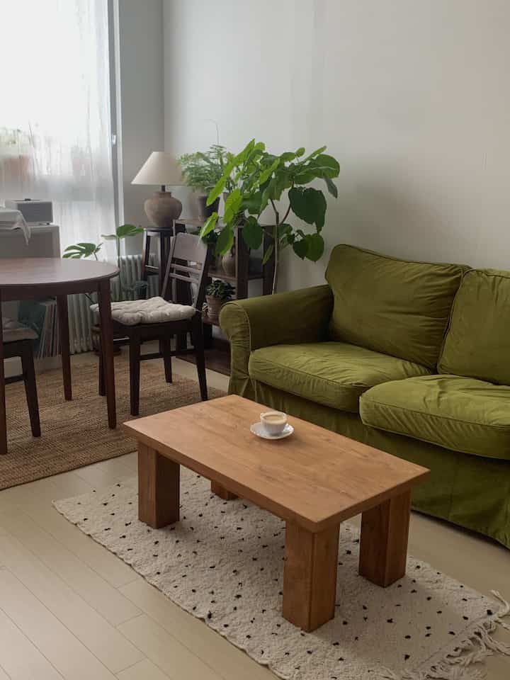 ナチュラルな木目調と緑のソファが印象的なリビングルーム、ダイニングテーブルと植物が温かみのある雰囲気を演出