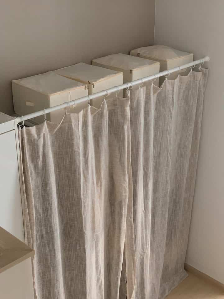 ベージュのリネンカーテンが設置されたワンルームの収納スペース、清潔感と自然な雰囲気のあるインテリア