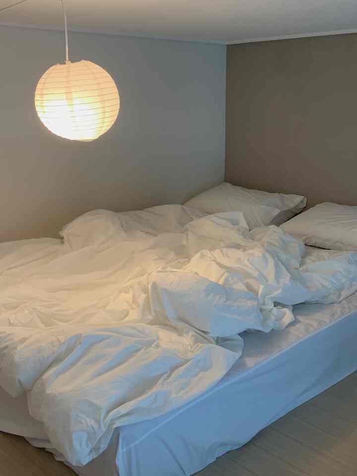 ホワイトとナチュラルな色調の寝室、和紙のペンダントライトと白い寝具が配置された雰囲気のある空間