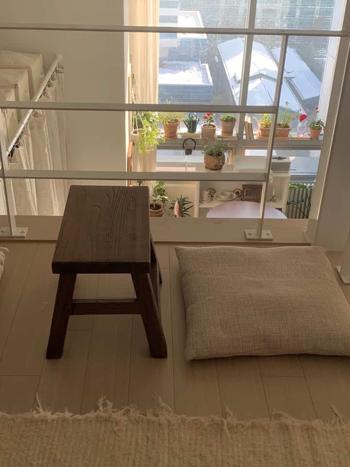 ナチュラルな色調のロフト玄関、木製スツールとベージュのクッション、様々な植物が配置され、落ち着いた雰囲気のあるインテリア