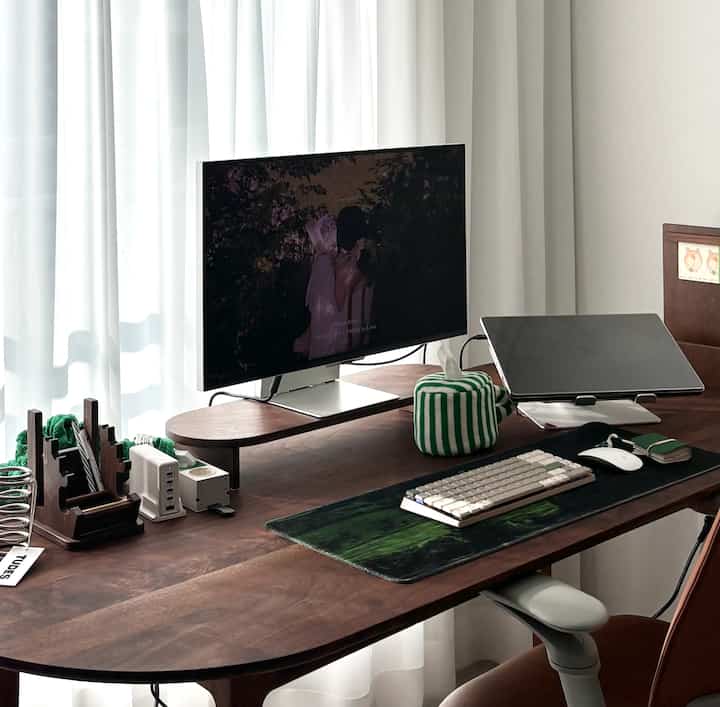 木目調のホームオフィス、モニター台を備えた広いデスクと緑のアクセントが配置された整った作業空間