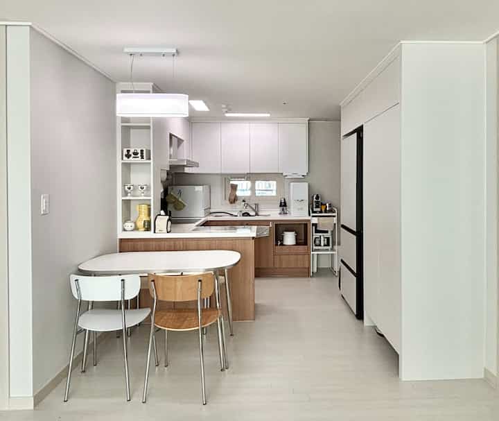 白と木目調の組み合わせが特徴的な狭いキッチン、ダイニングテーブルと改装されたパントリーが配置された爽やかな空間