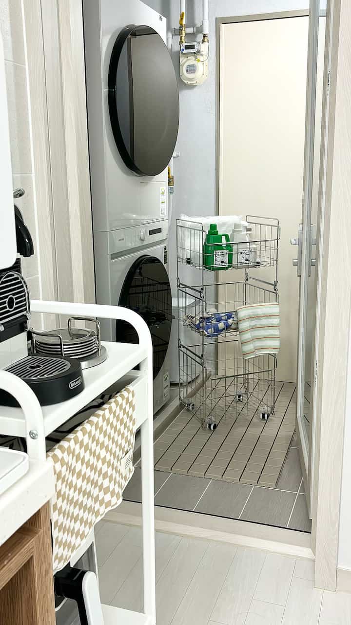 白とグレーのトーンのランドリールーム兼ベランダ、スタック型洗濯機と多段収納バスケットが配置された実用的な空間