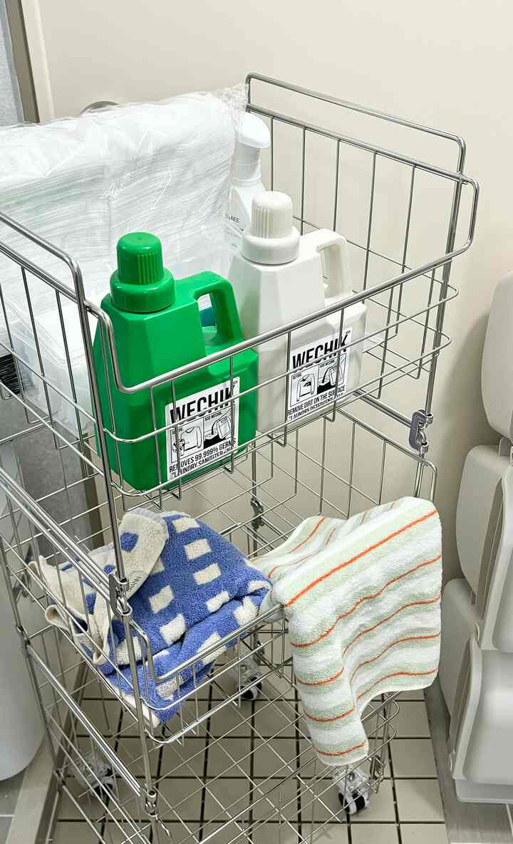 白い壁とシルバーのメタル収納カートが配置されたコンパクトなランドリールーム、タオルと洗剤が整頓された清潔感のある空間