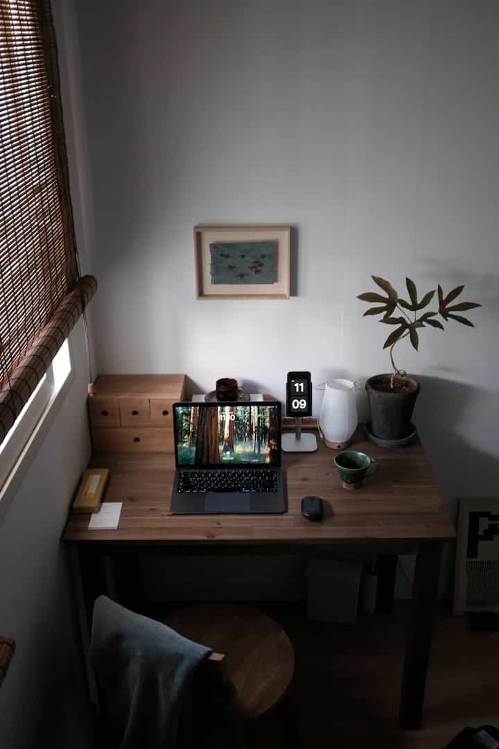 ナチュラルな木目調のホームオフィス空間、ノートパソコンと植物、額縁が配置された落ち着いた作業環境