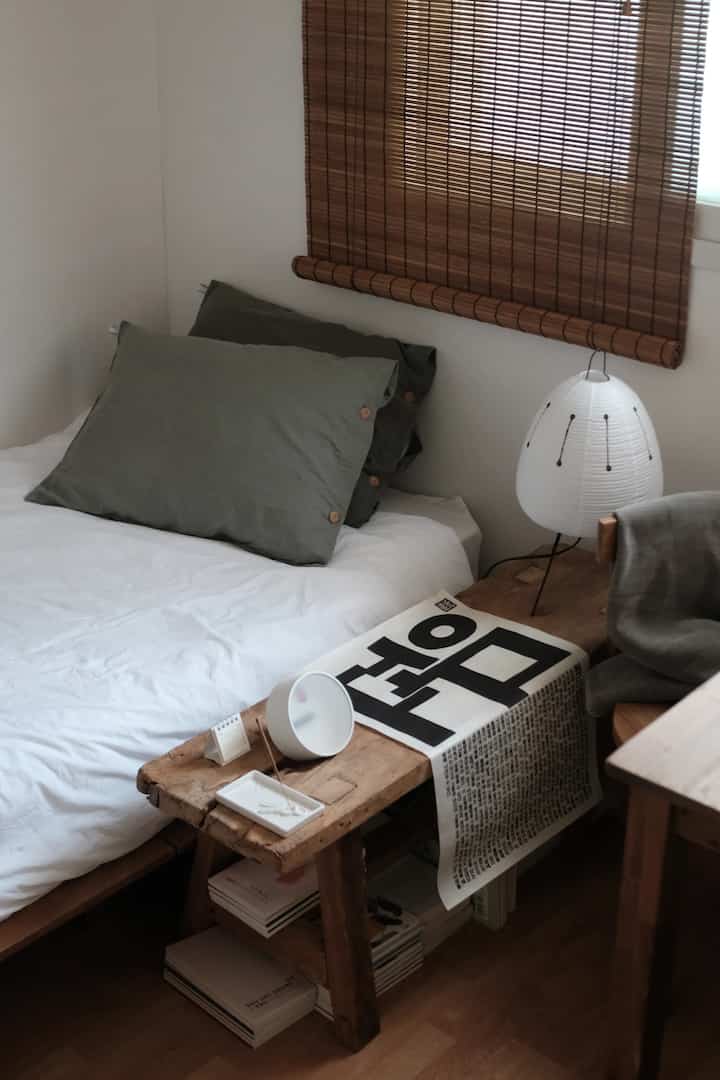 ナチュラルな木目調と白を基調とした寝室、枕とランプが配置された落ち着いた雰囲気のインテリア