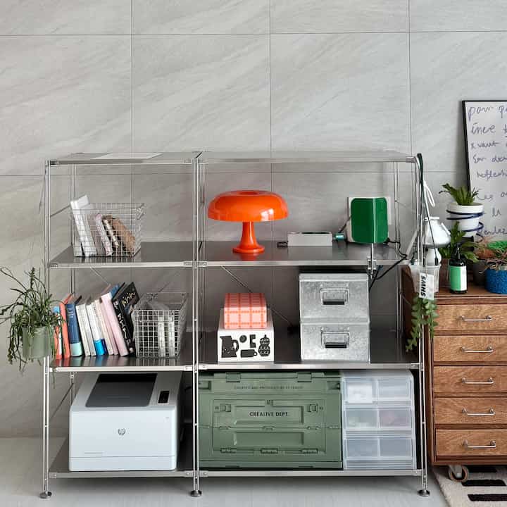 グレーとシルバーの色調の空間、中央にステンレス製の棚とオレンジ色のランプが配置された、すっきりとしたモダンなインテリア