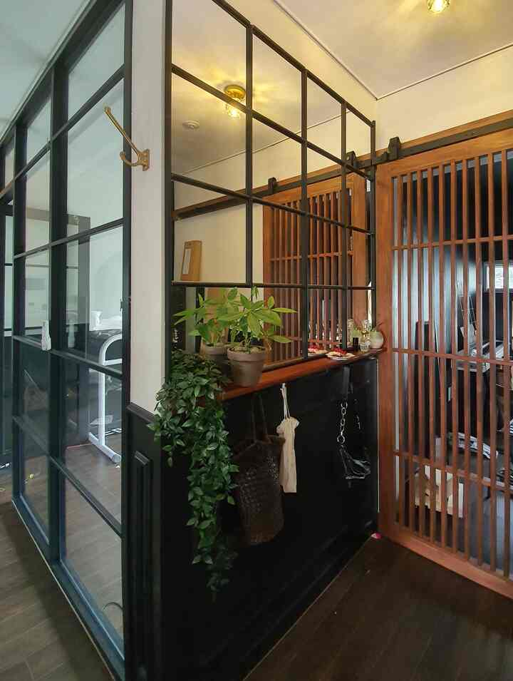 白と黒のトーンの狭い玄関、引き戸と格子の鏡、植物が配置された雰囲気のあるインテリア