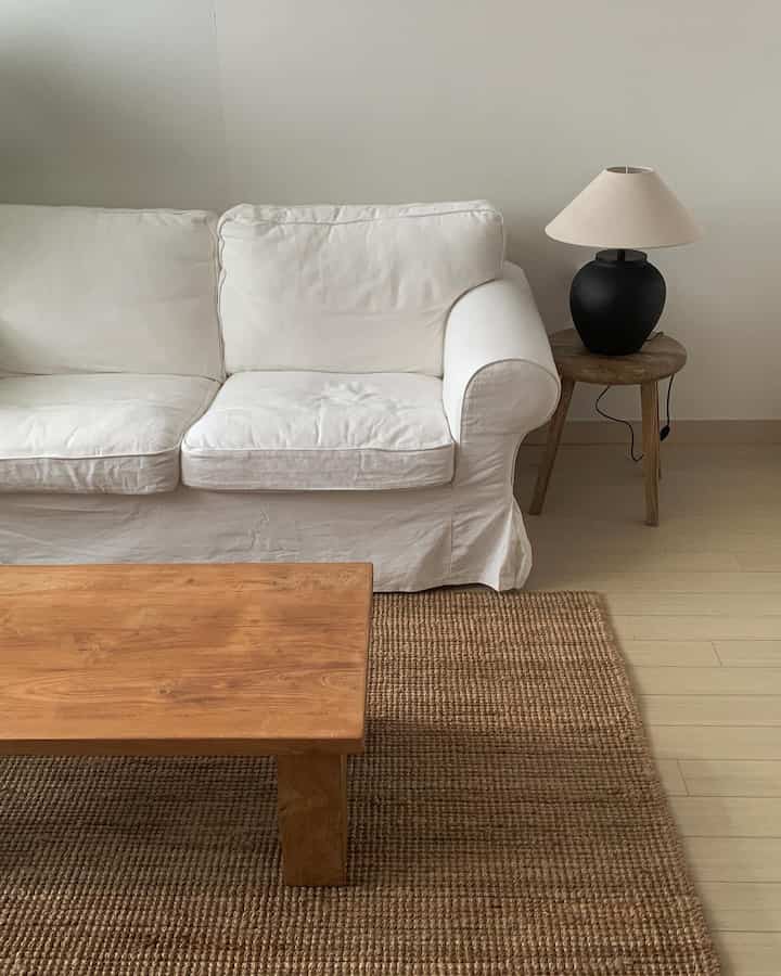 ナチュラルな色調のリビングルーム、白いソファと木製のコーヒーテーブル、ジュートのラグ、陶器のテーブルランプが配置された温かみのあるインテリア