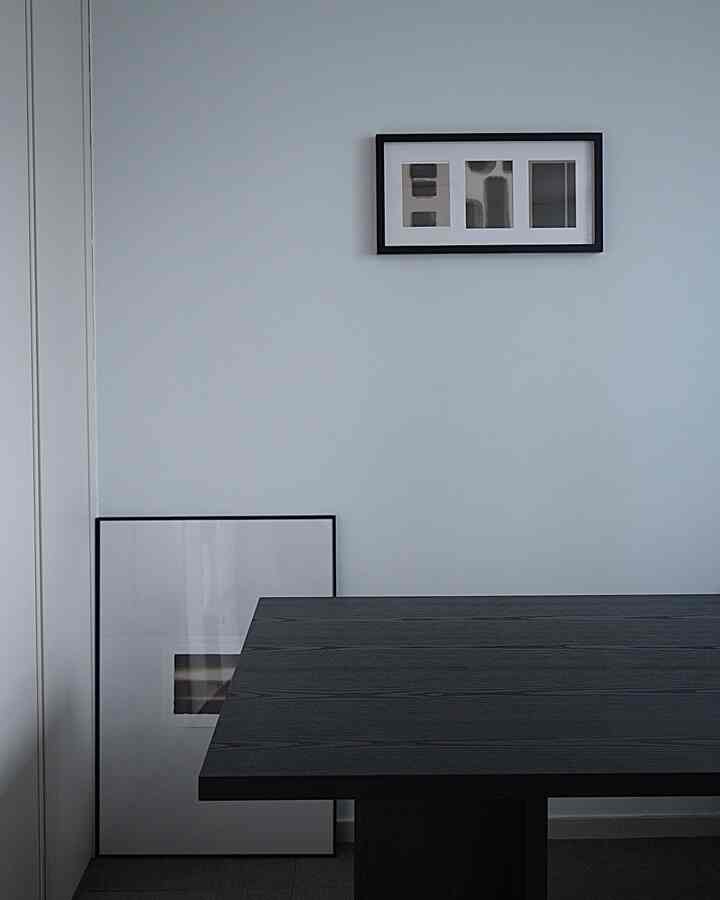 白い壁とダークグレーのテーブルが配置されたシンプルなダイニング、2つの額縁がある落ち着いた雰囲気のインテリア