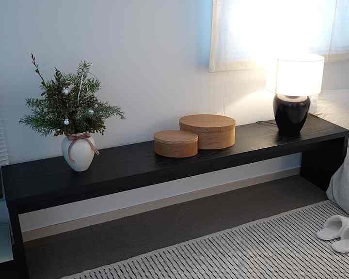 ブラックの木目調の寝室ナイトテーブルにシェーカーボックスとテーブルランプが配置されたシンプルな空間