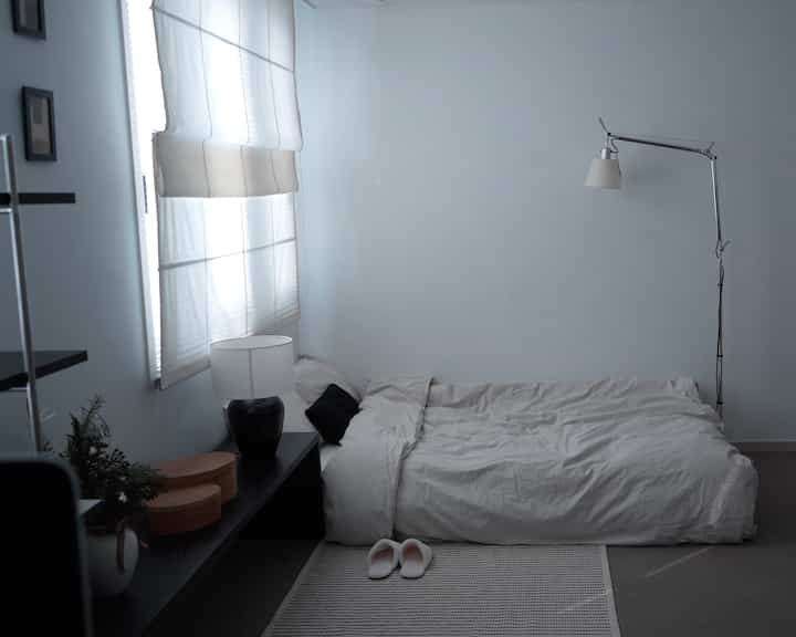 ホワイトトーンのシンプルモダンな寝室、ロータイプベッドとフロアランプが配置された清潔感のある空間