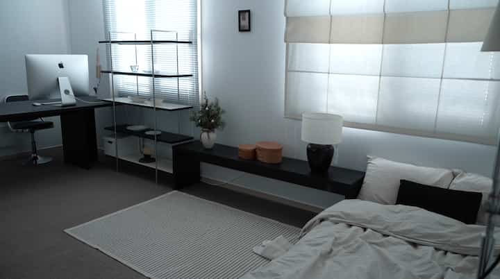 白と黒のトーンのモダンなホームオフィス兼寝室、机とベッドがすっきり配置された落ち着いた雰囲気のインテリア