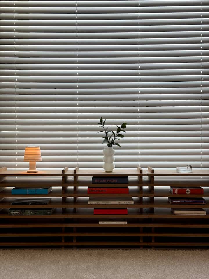 明るいホワイトトーンのリビングルーム窓辺に自然な木目調の棚が配置された清潔感のある北欧風インテリア