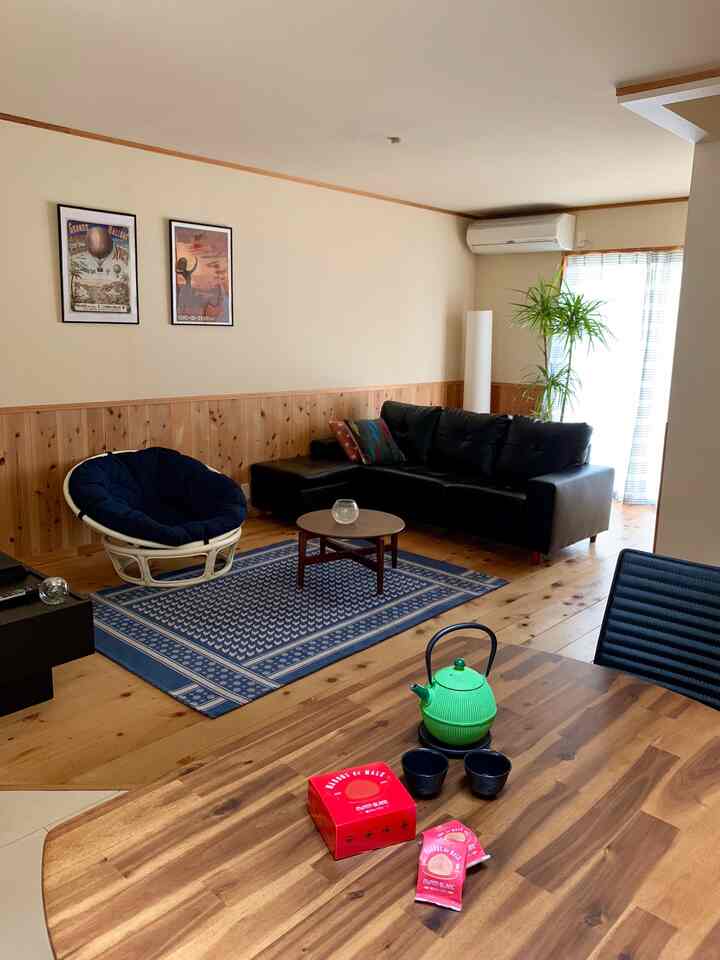 木目調の床と壁が印象的なナチュラルなリビング、黒いソファとネイビーブルーのラグが落ち着いた雰囲気を演出