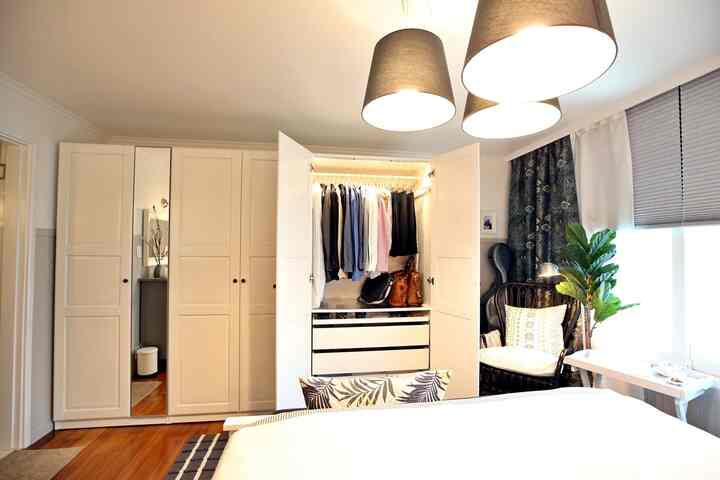 白を基調とした寝室、中央に開いた白いクローゼットが配置され、自然な木製の床やカーテン、観葉植物が調和した雰囲気のあるインテリア