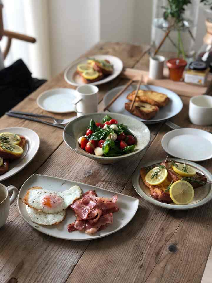 ナチュラルなブラウン色調のダイニングテーブルに朝食が並ぶ、ホームパーティーの雰囲気あるインテリア