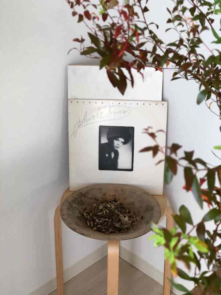 ナチュラルな木目調と白色のダイニングのコーナー、スツールの上にポプリとレコード、壁に絵が配置されたミニマルな雰囲気のインテリア