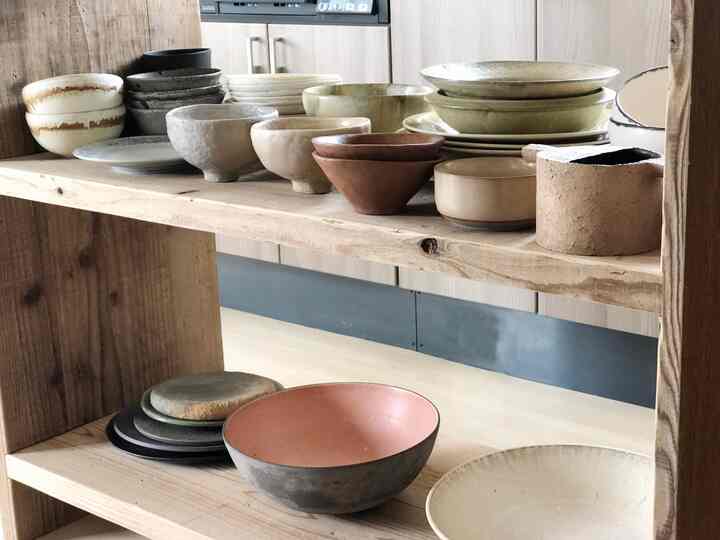 明るい木目調の棚に多様な色とデザインの陶器のボウルが整然と並べられたシンプルなキッチンインテリア