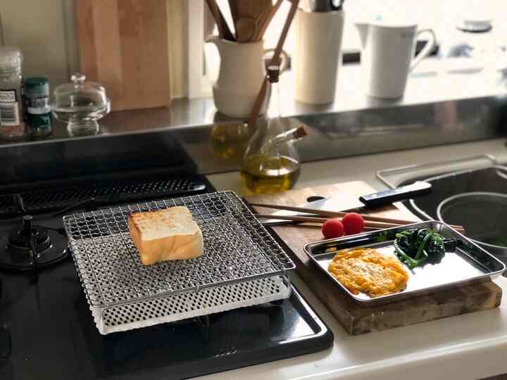 白とステンレスのトーンのキッチン、トーストと調理器具が配されたシンプルで落ち着いた雰囲気のインテリア