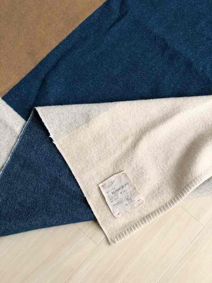 深い青とベージュのリミテッドカーペットが明るい木目調の床に広げられた、シンプルでナチュラルな寝室のインテリア