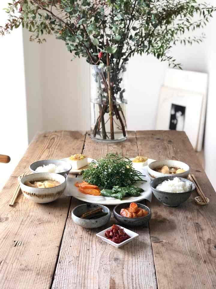 ナチュラルな色調のダイニングルーム、木製のダイニングテーブルに直線的な陶器セットとグラスコの丸形花瓶が配置された落ち着いた食事空間