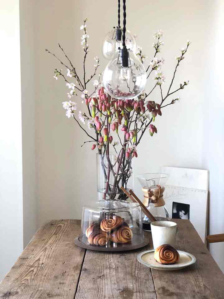 ナチュラルな色調のダイニングルーム、透明なガラス花瓶に季節の花が飾られ、木製の食卓にコーヒー器具が配置された雰囲気のあるインテリア