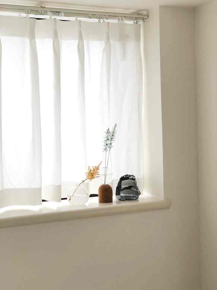 柔らかな白色の寝室の窓辺、透明なガラス花瓶と小さなオブジェが配置されたシンプルな空間