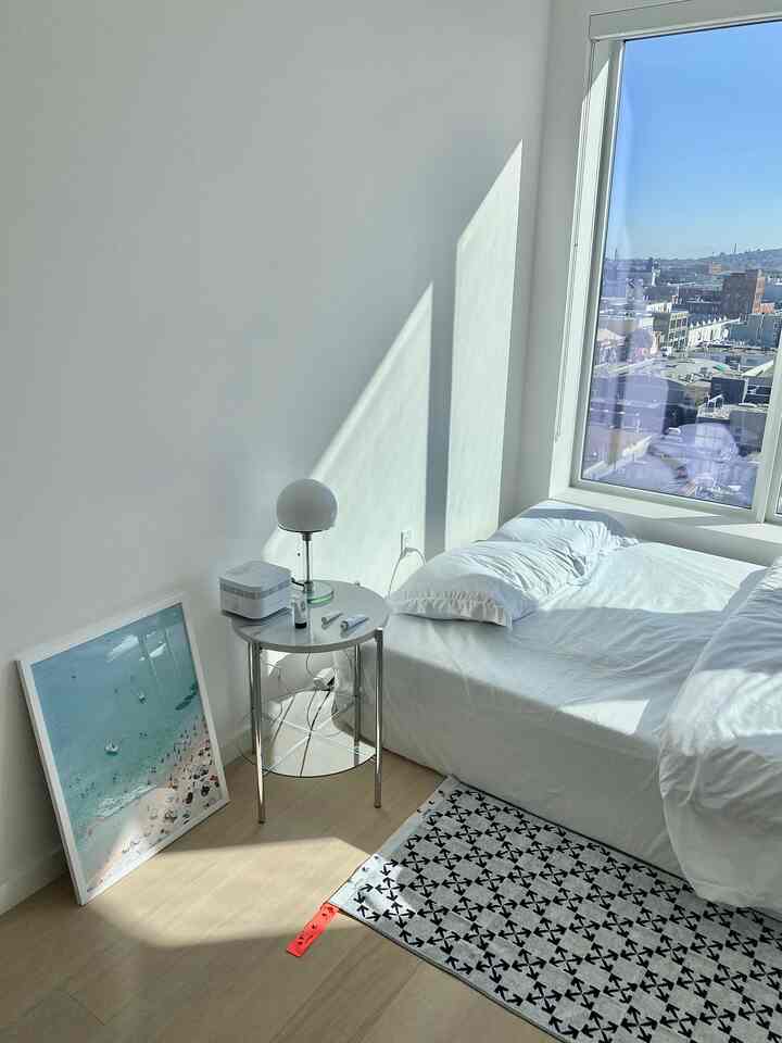 ホワイトとナチュラルな木目調の寝室、ナイトテーブルと青いポスターが配置された明るくすっきりとした雰囲気のインテリア