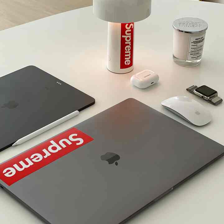 白いテーブルにシルバーのアップル製品とキャンドルが配置されたモダンなホームオフィス空間