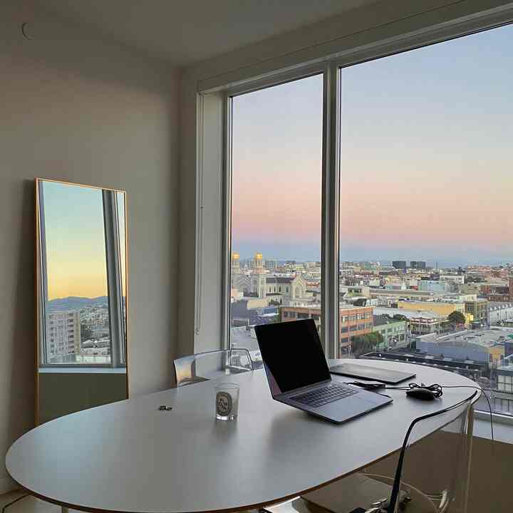 白と透明のトーンが特徴のミニマルなリビング、夕焼けを映す全身鏡とノートパソコンのある清潔なテーブル空間