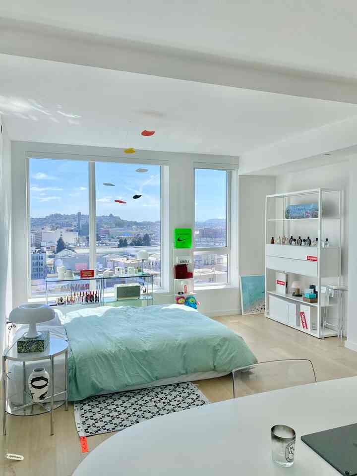 ホワイトとナチュラルカラーの寝室、窓際にデスクと透明な椅子が配置されたシンプルでミニマルな雰囲気のインテリア