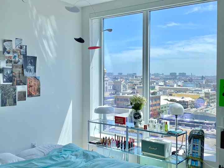 明るいホワイトとブルーのトーンの寝室、大きな窓のそばにガラスの棚とテーブルランプが配置された清潔でスタイリッシュな空間