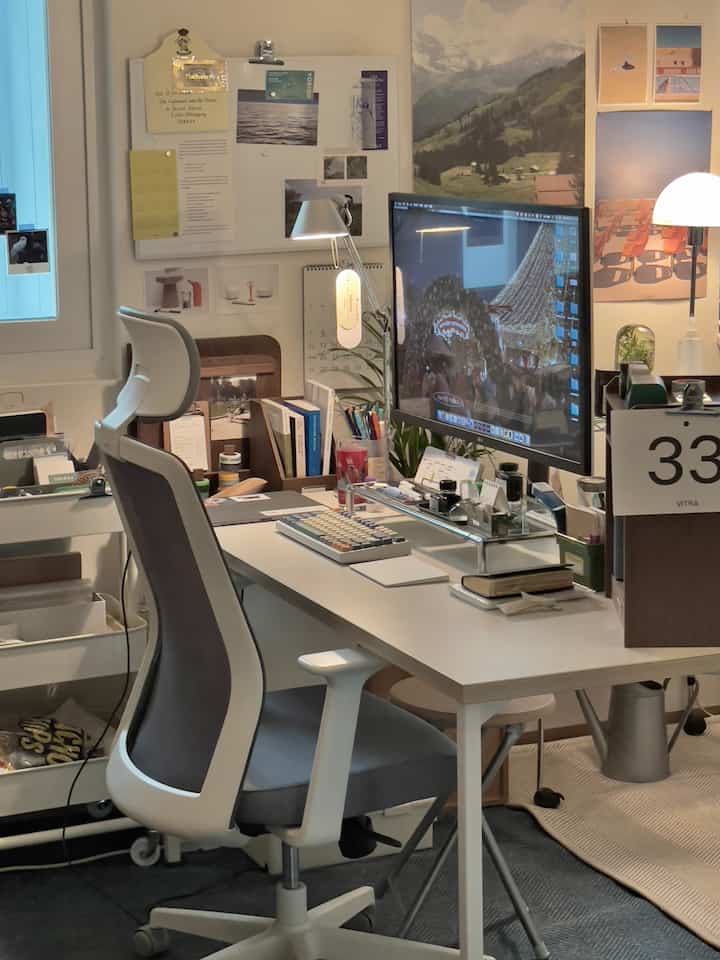 ナチュラルカラーのホームオフィス、ホワイトのデスクとグレーのオフィスチェア、大型モニターとテーブルランプが配置された落ち着いた作業空間