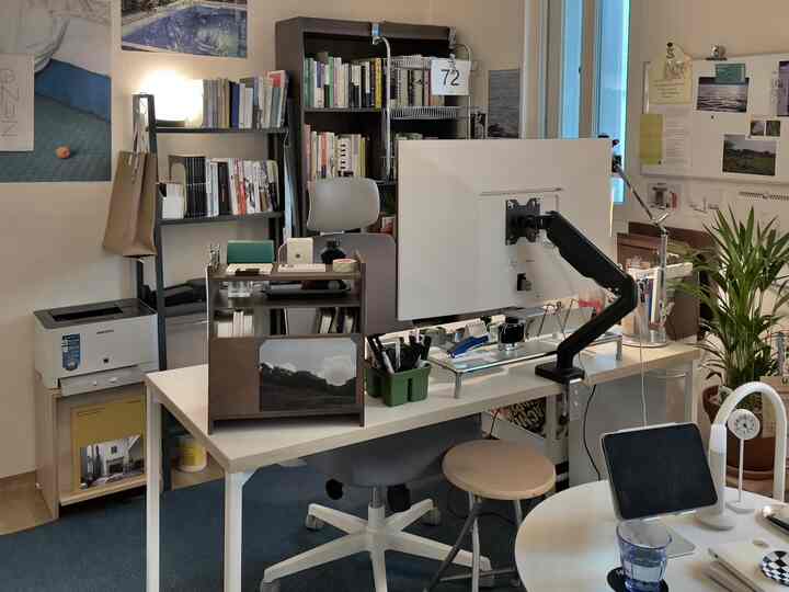 落ち着いた青いカーペットと白いデスク、オフィスチェア、整理された本棚や棚が配置されたホームオフィスの空間