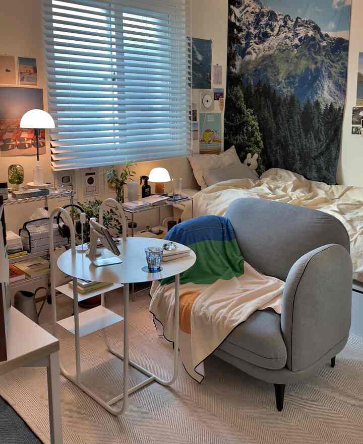 白とベージュの色調のワンルーム寝室、1人用ソファとデスク、ベッドが配置された居心地の良い多目的スペース