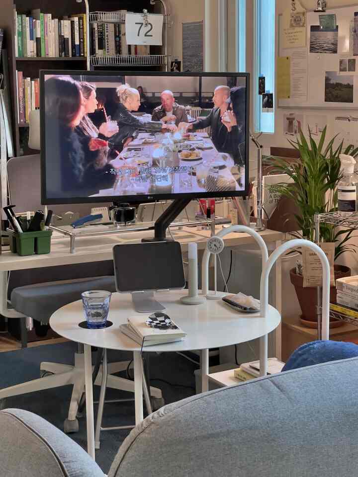 ホワイトとグレーの色調のリビング兼ホームオフィス、 大型モニターとデスク、ソファ、植物が配置された雰囲気のあるインテリア