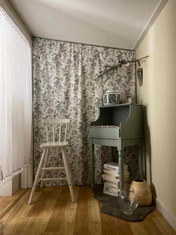 ナチュラルなベージュとグリーンの色調の狭い部屋、花柄カーテンと淡いグリーンのコンソール、アイボリーの椅子が配置された雰囲気のあるインテリア