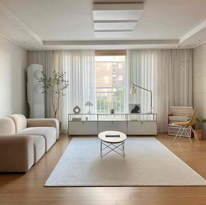 ホワイトとベージュのトーンが調和するリビング、ファブリックソファとラグ、USMシェルフ、シアーカーテンが心地よい空間を演出