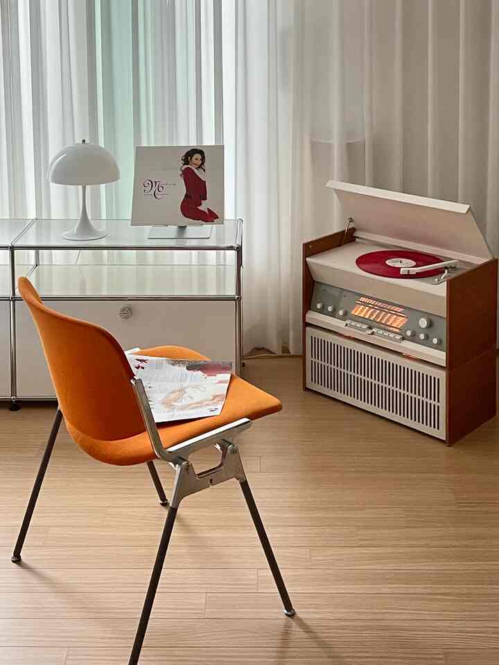 明るいオレンジの椅子と白いカーテン、赤いターンテーブルが配置されたモダンでレトロな雰囲気のリビング