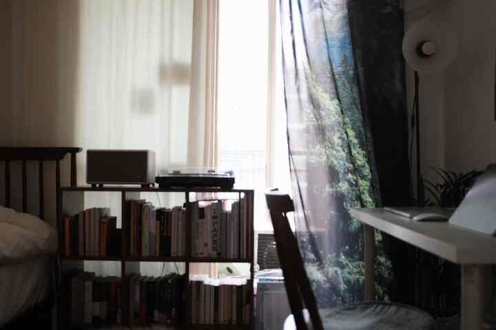 ホワイトとブラウンの調和がとれた寝室兼書斎、書棚と木製家具が配置された居心地の良いコンパクトな空間