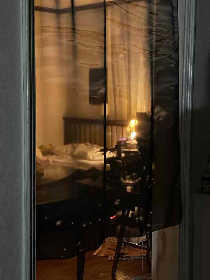 暖かい照明と黒いカーテンのある白色調の寝室、居心地の良いベッドとナイトテーブルが配置された雰囲気のあるインテリア